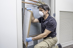 HVAC tech wearing mask and gloves changing an air filter